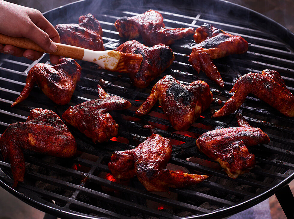 Chicken wings on a grill being basted