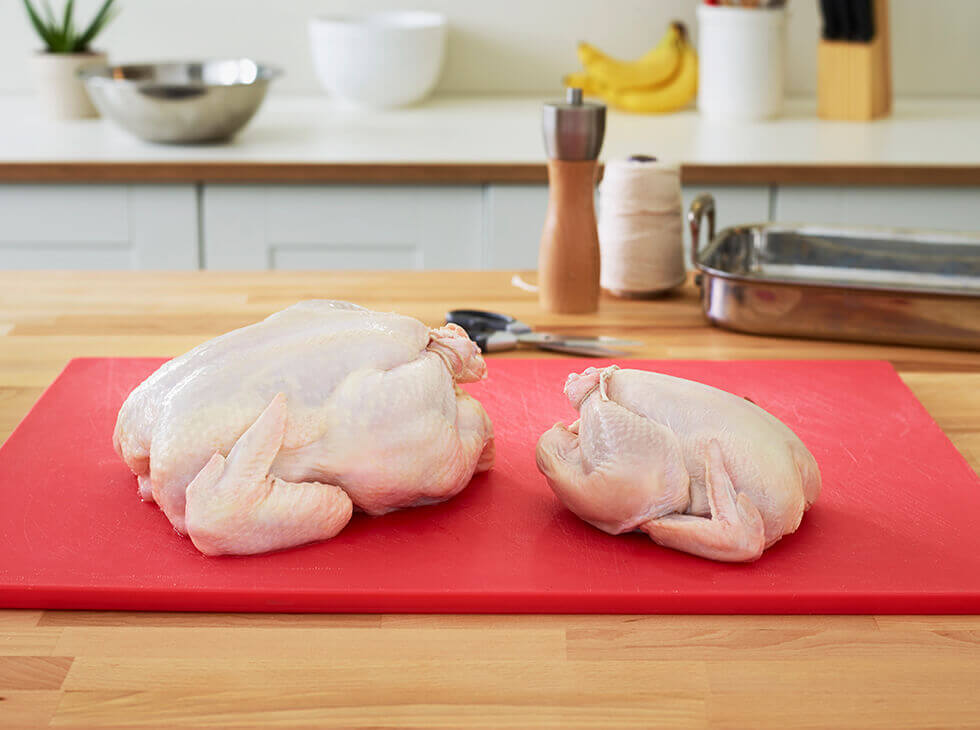 Whole chicken and Cornish hen on a red cutting board